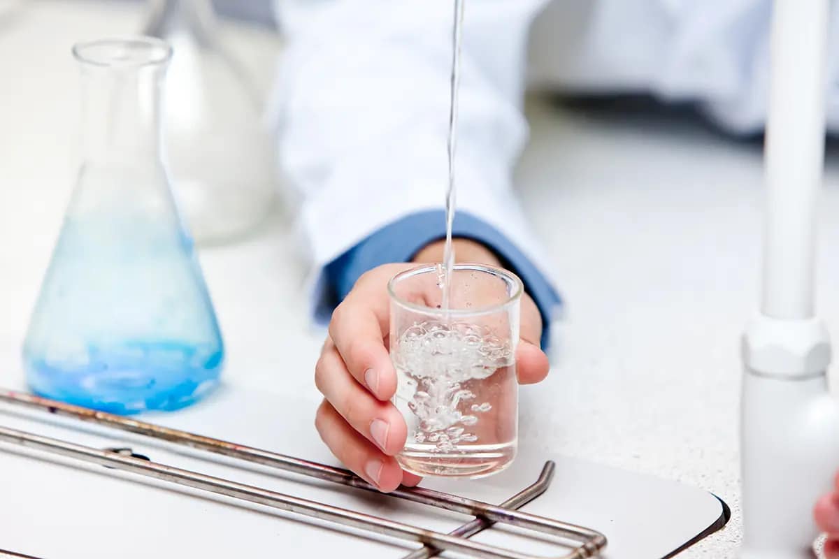 Analista chimico in camice bianco versa un campione d'acqua in un cilindro di vetro durante un test di analisi acqua
